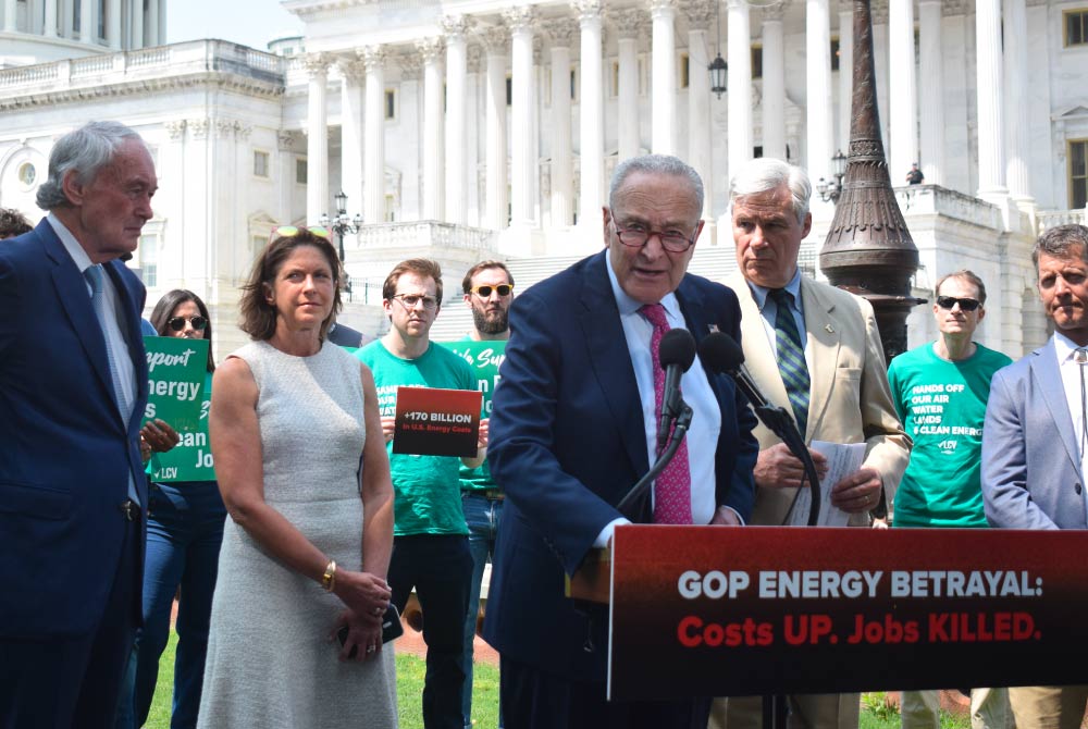 Senator Chuck Schumer speaks at a podium in front of the Capitol building, flanked by other members of Congress and LCV staff