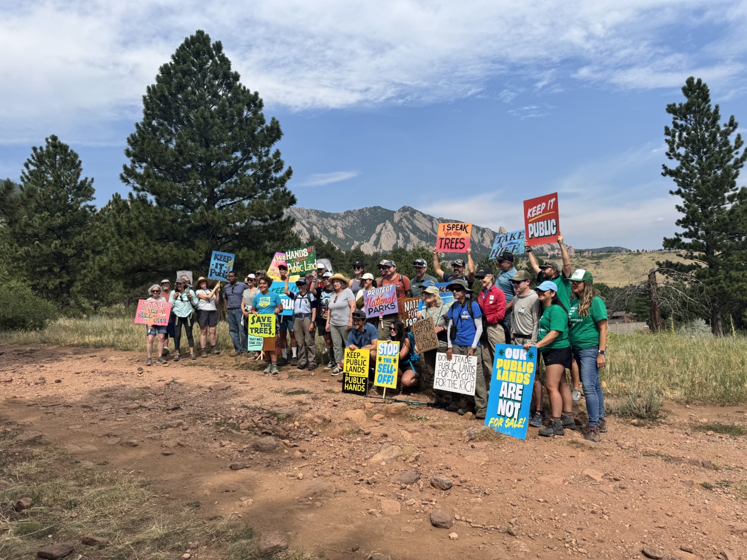 A group of people pose holding signs with a mountain in the background.