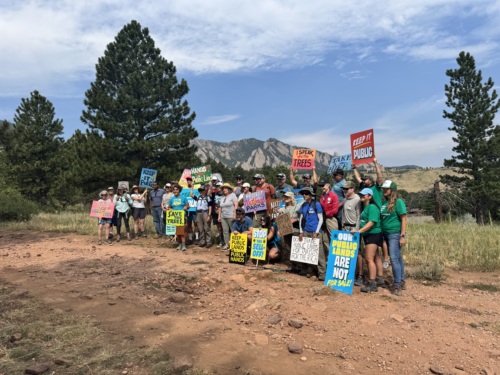 A group of people pose holding signs with a mountain in the background.