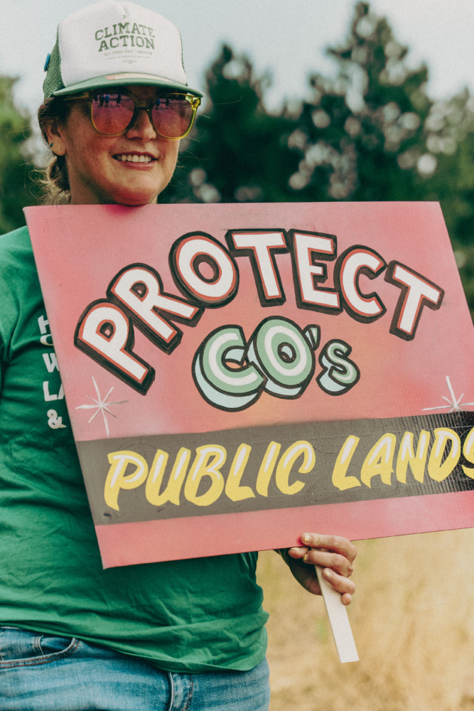 A woman holds a sign reading "Protect CO's Public Lands."