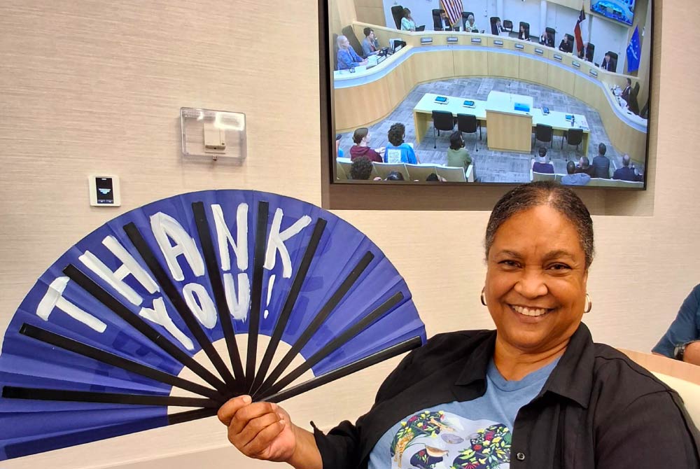 A woman smiles while holding a fan that reads “thank you”
