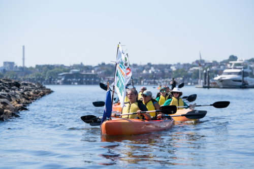 People in kayaks on a body of water with a city in the background.