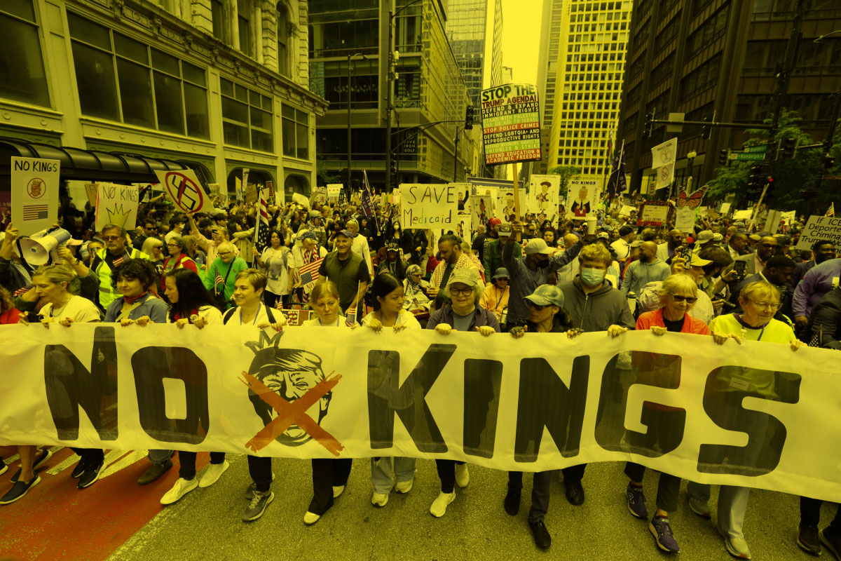 Protestors carry a banner that reads “No Kings” and features an image of Trump wearing a crown with an X covering his face.