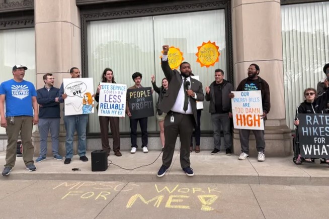 Michigan state representative Donavan McKinney speaks in front of a line of people holding signs.