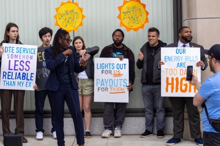 A line of people holding signs that oppose energy rate hikes.