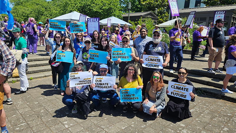 A group of people pose for a photo holding signs supporting various climate programs.