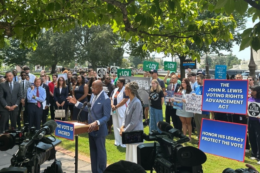 Sen. Warnock speaks at a podium outdoors surrounded by supporters.
