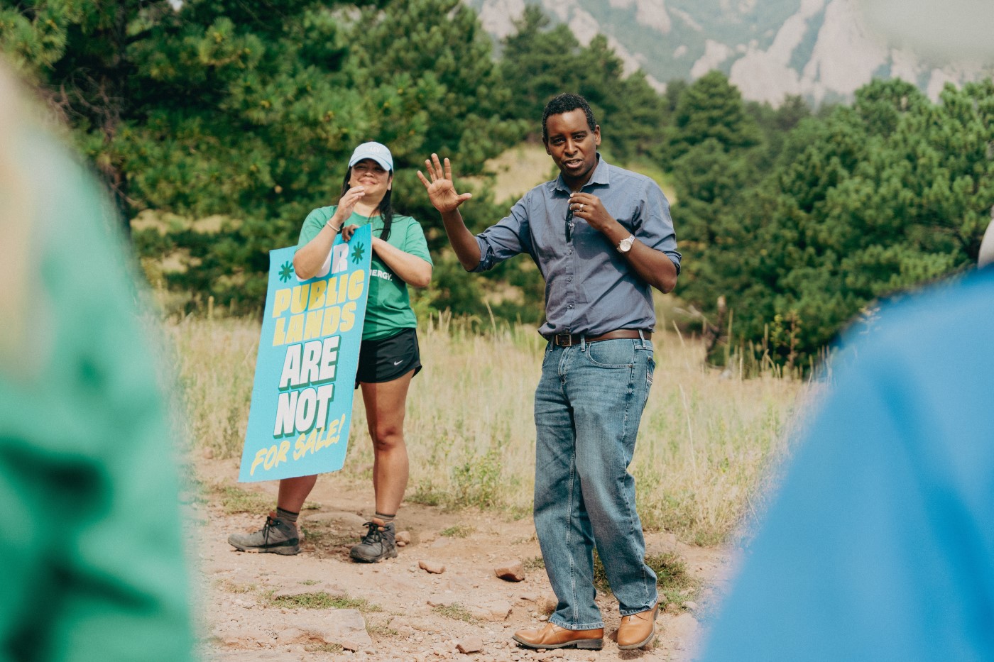Rep. Neguse speaks on trail with a mountain view in the background.