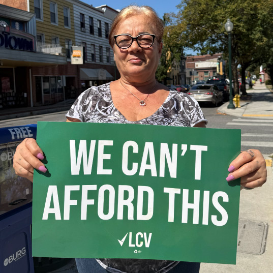 Denise holds a "We Can't Afford This" sign
