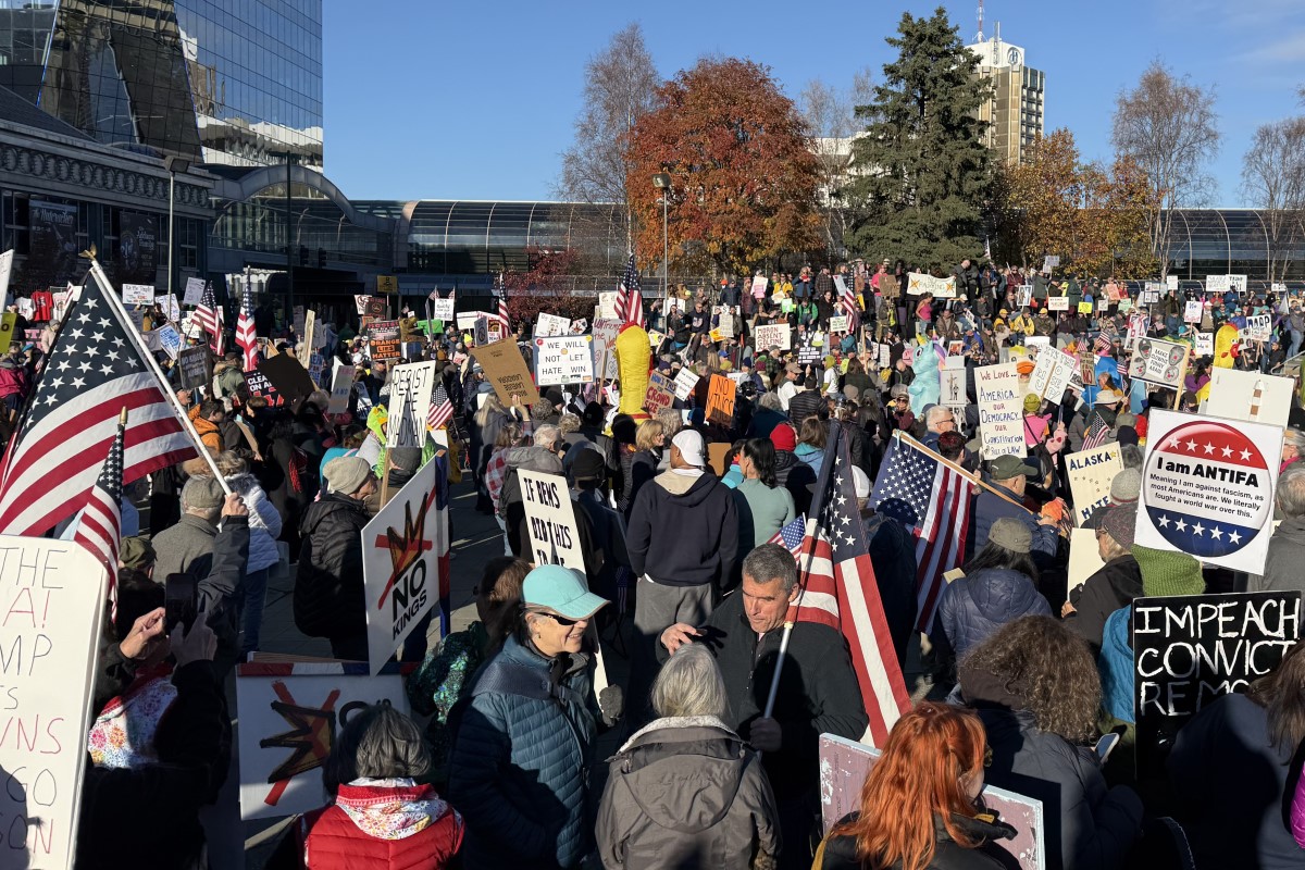 A crowd bundled in jackets and carrying American flags and protest signs at an autumn rally in downtown Anchorage.