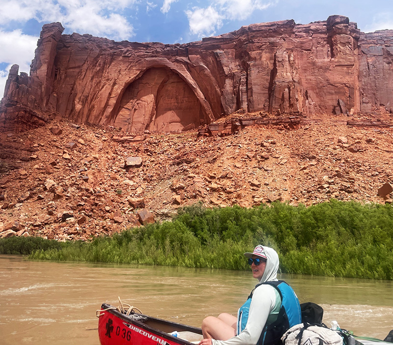 A person kayaks in front of a red rock formation.