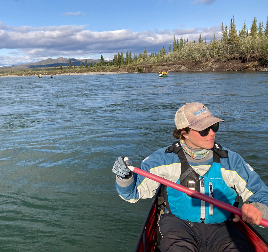 A woman kayaks with trees in the background.
