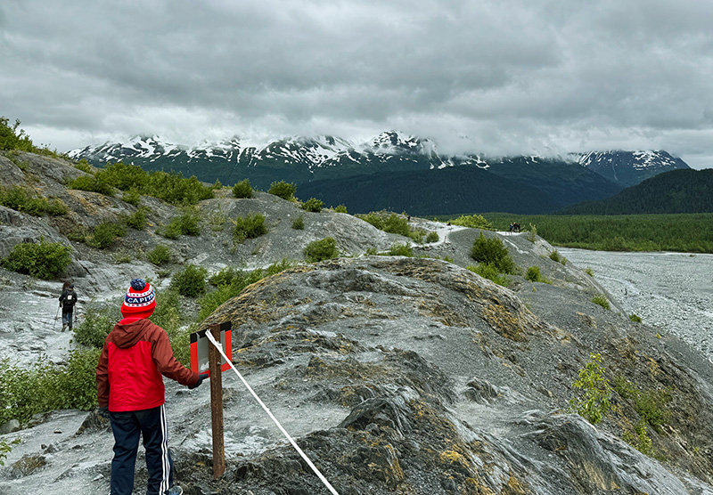 A rocky landscape with mountains in the background and a child in a red coat in the foreground.