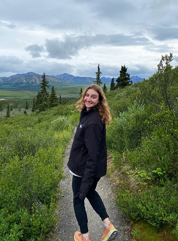 A woman stands in a green landscape.